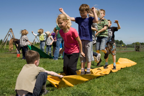 Des enfants jouent dehors sur l’herbe au Boerderij De Boerinn – Safaritenten Utrecht sous le soleil estival.