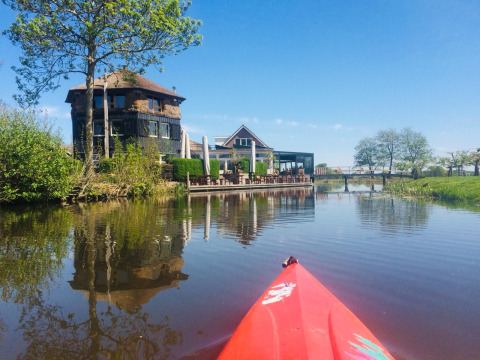 Un kayak rouge sur l'eau en direction du glamping Boerderij De Boerinn avec terrasse à Utrecht, Pays-Bas.
