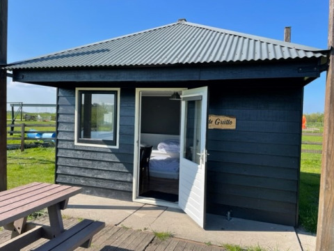 Schwarze Glampinghütte bei Boerderij De Boerinn – Safaritenten Utrecht mit offener Tür und Picknickbank.