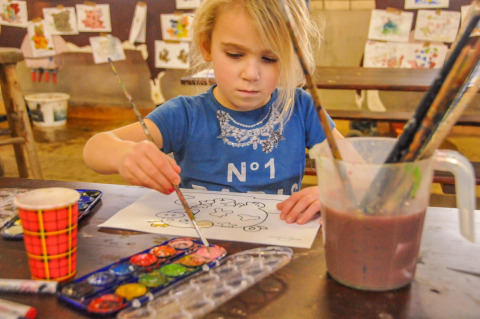 Niña pintando una hoja para colorear con acuarelas y pinceles en Boerderij De Boerinn – Safaritenten Utrecht.