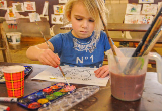 Enfant peignant une page avec des aquarelles et des pinceaux chez Boerderij De Boerinn – Safaritenten Utrecht.