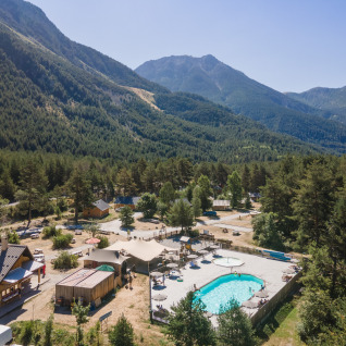 Vue aérienne du Huttopia La Clarée - Glamping Hautes-Alpes avec piscine, arbres et montagnes autour.