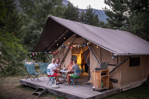 Hébergement glamping Huttopia La Clarée, Hautes-Alpes, avec des hôtes profitant de la terrasse du tente.