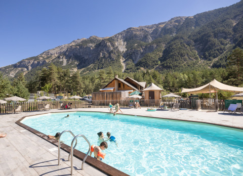 Familias disfrutan de la piscina en Huttopia La Clarée - Glamping Hautes-Alpes con vistas a las montañas.