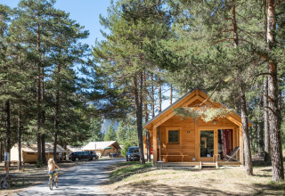 Cabaña de madera y tiendas entre pinos en Huttopia La Clarée - Glamping Hautes-Alpes, niña en bicicleta.