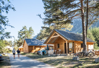 Cabañas de madera y visitantes en Huttopia La Clarée - Glamping Hautes-Alpes, perfecto para acampar con estilo.