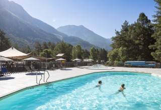 Enfants nageant dans une piscine extérieure avec vue sur les montagnes à Huttopia La Clarée Glamping, Hautes-Alpes.