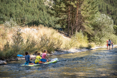 Enfants pagayant sur une planche SUP à Huttopia La Clarée Glamping, entourés de nature alpine.