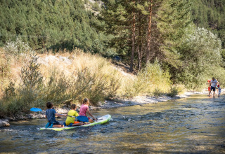 Bambini su una tavola SUP pagaiando nel fiume a Huttopia La Clarée Glamping, immersi nella natura.
