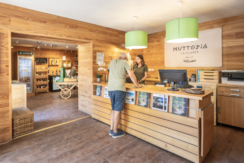 Recepción de Huttopia La Clarée Glamping Hautes-Alpes con decoración de madera y huésped en el mostrador.