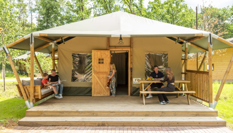 Family relaxing on the porch of a luxury glamping tent at Serengeti Park Tongasoa Lodges, Niedersachsen, Germany.