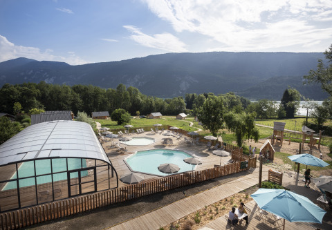 Blick auf Huttopia Lac d'Aiguebelette Glamping mit Pool, Sonnenschirmen und Bergen im Hintergrund.
