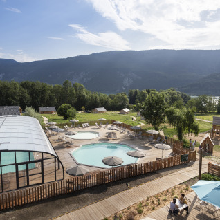 Vista panorámica de Huttopia Lac d'Aiguebelette glamping con piscina, sombrillas y paisajes de montaña.