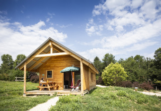 En træhytte med terrasse og parasol på Huttopia Lac d'Aiguebelette Glamping i naturskønne Savoie.
