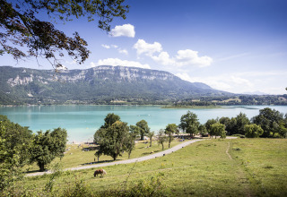 Panoramic view of Huttopia Lac d'Aiguebelette - Glamping Savoie lake, surrounded by mountains and meadows.