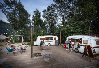 Outdoor glamping area at Huttopia Lac d'Aiguebelette with vintage caravans, string lights and guests relaxing.