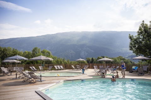 Buitenzwembad met ligbedden en parasols bij Huttopia Lac d'Aiguebelette Glamping Savoie met uitzicht op de bergen.