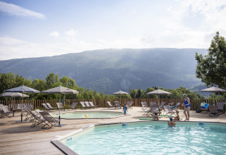 Udendørs poolområde med liggestole og parasoller på Huttopia Lac d'Aiguebelette Glamping Savoie med udsigt til bjerge.