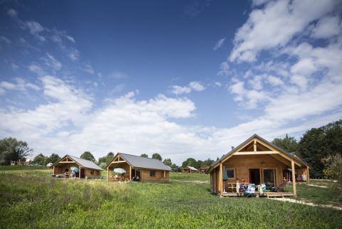 Gemütliche Holzhütten bei Huttopia Lac d'Aiguebelette - Glamping Savoie, umgeben von Natur und blauem Himmel.