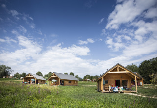Gemütliche Holzhütten bei Huttopia Lac d'Aiguebelette - Glamping Savoie, umgeben von Natur und blauem Himmel.