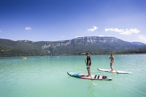 Zwei Personen paddeln auf Boards auf einem See mit Blick auf die Berge, Huttopia Lac d'Aiguebelette.