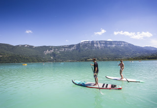 Zwei Personen paddeln auf Boards auf einem See mit Blick auf die Berge, Huttopia Lac d'Aiguebelette.