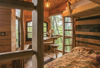 Cozy glamping treehouse with wood interior, double bed, writing desk, and forest views.