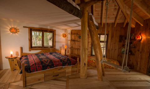 Rustikale Baumhaus-Glamping-Unterkunft mit Holzinterieur, Doppelbett und Schaukel im Robins Nest, Hessen.