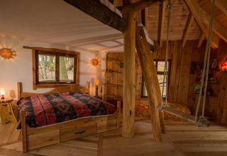 Rustikale Baumhaus-Glamping-Unterkunft mit Holzinterieur, Doppelbett und Schaukel im Robins Nest, Hessen.
