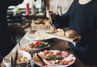 Guest preparing breakfast with bread, cheese, meat, and veggies at Baumhausherberge Robins Nest glamping.
