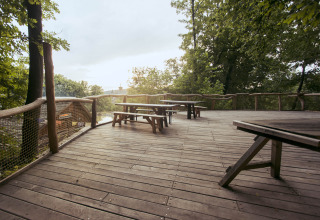 Große Holzterrasse mit Picknicktischen im Baumhausherberge Robins Nest, umgeben von Bäumen in Hessen.