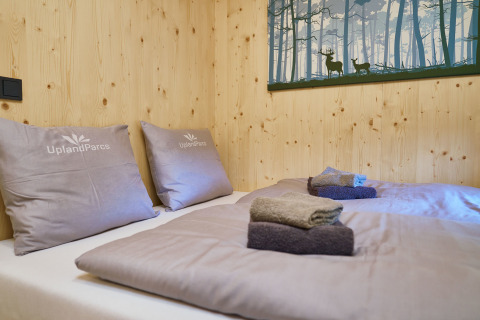 Knusse slaapkamer bij UplandParcs Sauerland Boomhutten met houten wanden, kussens en gevouwen handdoeken op bed.