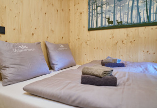 Knusse slaapkamer bij UplandParcs Sauerland Boomhutten met houten wanden, kussens en gevouwen handdoeken op bed.