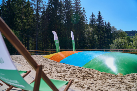 Area glamping all'aperto a UplandParcs Sauerland - Boomhutten con cuscino elastico colorato, sabbia e foresta vicino.