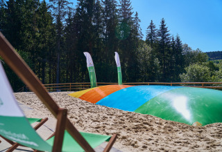 Glamping bij UplandParcs Sauerland - Boomhutten met kleurrijk springkussen, zand en bos op de achtergrond.
