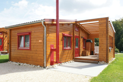 Houten bungalow met rode kozijnen op Camping & Vakantiepark Orsingen in Baden-Württemberg, perfect voor glamping.