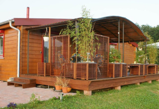 Wooden bungalow with covered terrace and potted plants at Camping & Vakantiepark Orsingen, Baden-Württemberg.