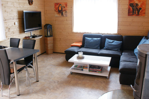 Sala moderna en bungalow de madera con sofá negro, TV de pantalla plana, mesa y cuadros decorativos.