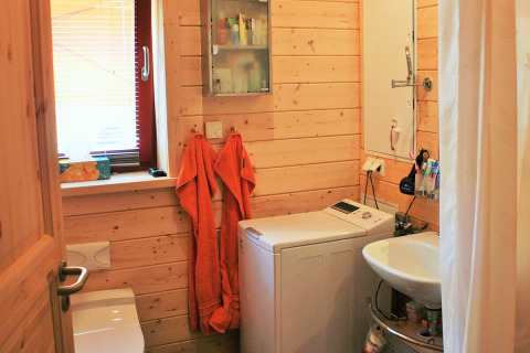 Small bathroom with wood-paneled walls, a washing machine, sink, and two orange towels in a glamping unit.