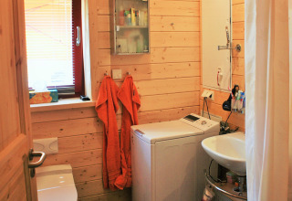 Bagno piccolo in bungalow glamping con pareti in legno, lavatrice, lavandino e due asciugamani arancioni.