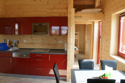 Modern glamping bungalow interior at Orsingen with red kitchen, dining area, bunk beds, and wood walls.