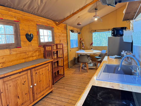 Interno di tenda glamping presso Agriturismo & Glamping Serraiola Alta con cucina, tavolo e arredo in legno.