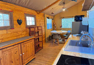 Interno di tenda glamping presso Agriturismo & Glamping Serraiola Alta con cucina, tavolo e arredo in legno.
