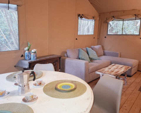 Interior de una tienda glamping en Serraiola Alta, Toscana, con sofá, mesa rústica y comedor junto a la ventana.