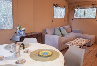 Innenansicht eines Glampingzeltes mit Sofa, Esstisch und Fenstern mit Waldblick bei Serraiola Alta in der Toskana.