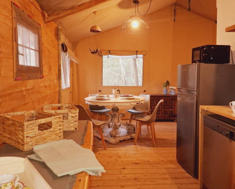 Vista interior de una acogedora tienda glamping con mesa de comedor, sillas, nevera y muebles de madera.