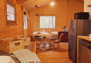 Vue intérieure d'une tente de glamping confortable avec table, chaises, réfrigérateur et bois naturel.