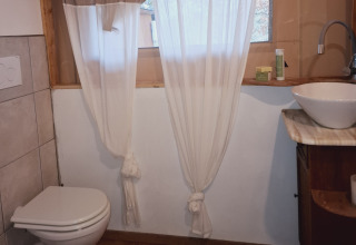 Salle de bain avec toilettes, lavabo et rideaux chez Agriturismo & Glamping Serraiola Alta en Toscane.