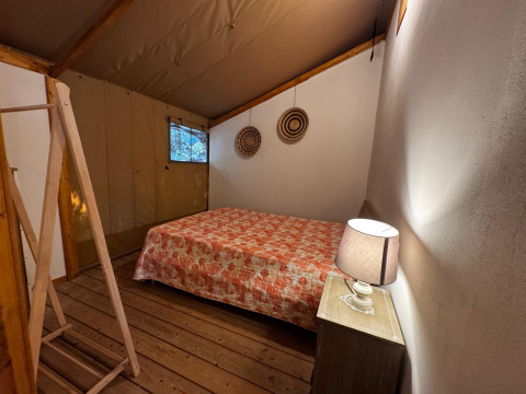 Habitación de tienda glamping en Serraiola Alta, Toscana, con cama doble, mesita de noche y lámpara suave.