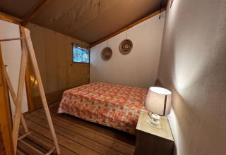 Camera da letto di una tenda glamping presso Serraiola Alta in Toscana con letto matrimoniale e abat-jour.